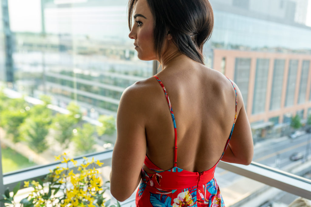 Female model wearing open back red jumpsuit with floral print.
