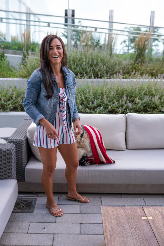 Female model wearing jean jacket with festive romper for the 4th of July holiday.